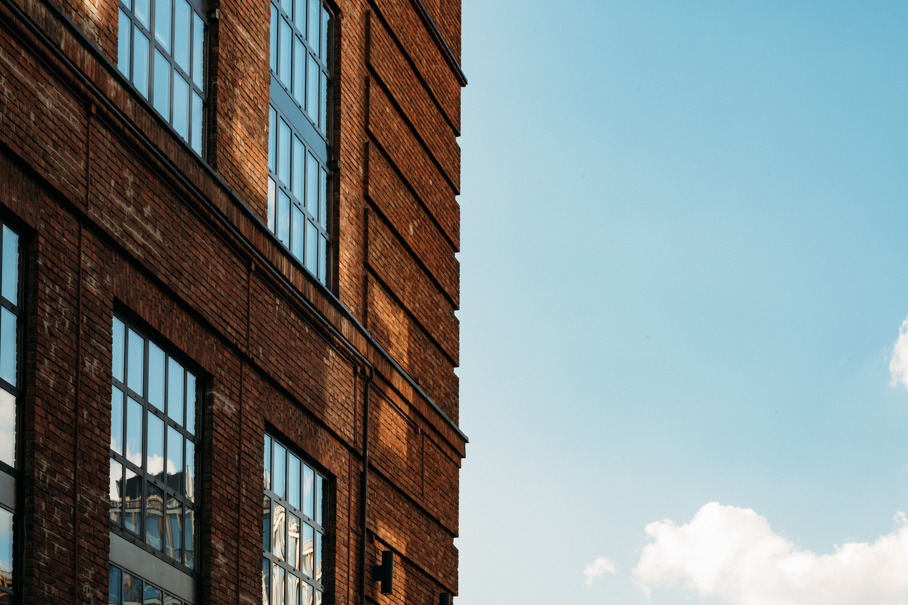 Close-up of a brick building with large windows reflecting the sky.