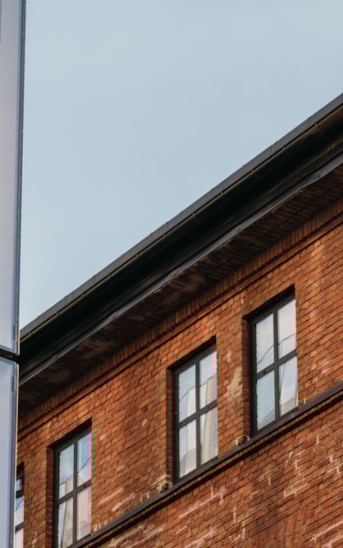 Närbild av detaljer av två byggnader. Glasbyggnad till vänster som skär diagonalt ner framför en brun tegelbyggnad till höger.