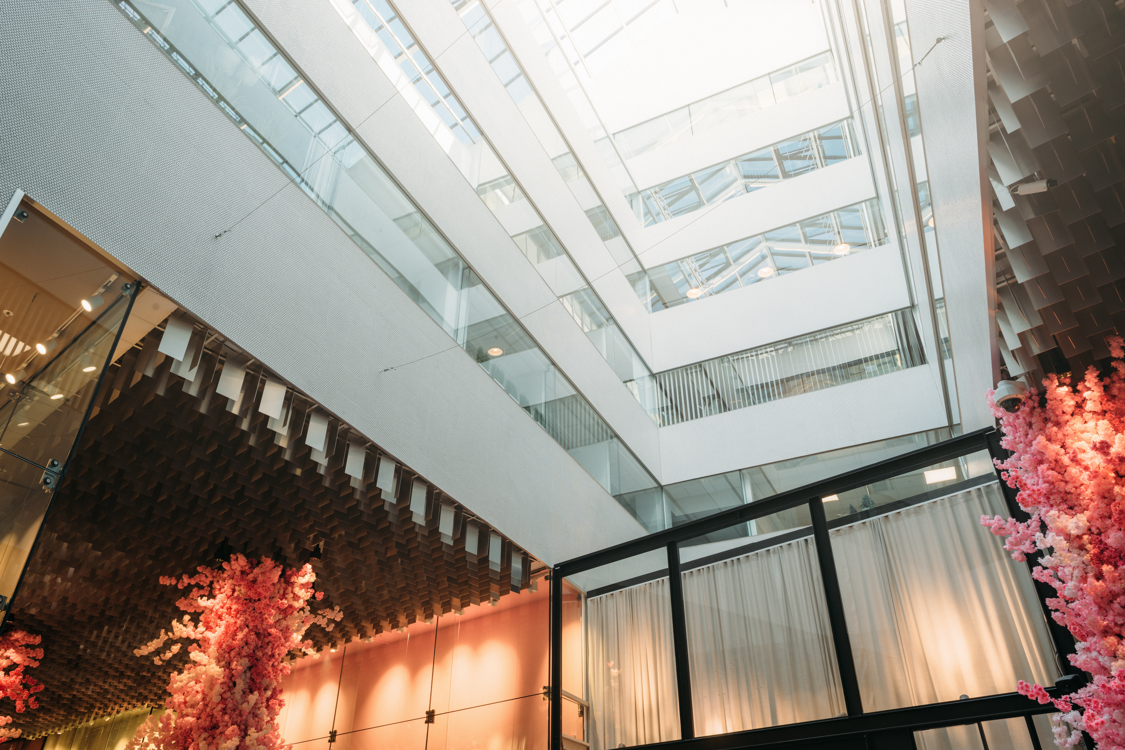 Close-up of a modern building interior with a glass ceiling, multiple floors, and pink floral decorations.